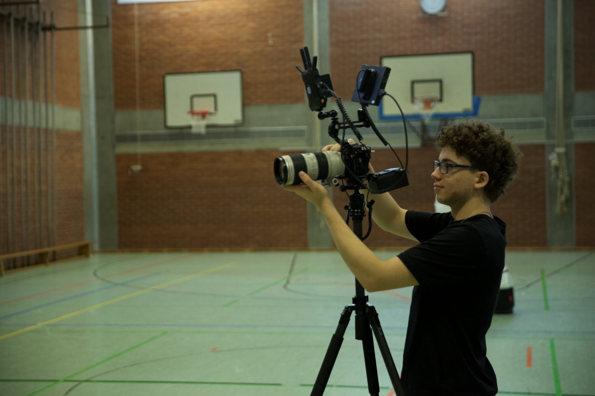Crew-Mitglied filmt mit Kamera auf dem Stativ in der Sporthalle